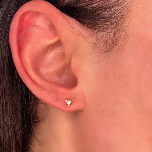A close-up image of a woman's ear wearing a gold triangle stud earring with a cubic zirconia stone.