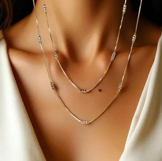 Close-up of a person wearing two gold necklaces on a blurred background