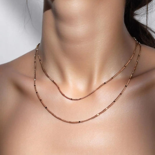 A close-up image of a woman's neck wearing a gold-filled curb chain necklace with a pressed detail.