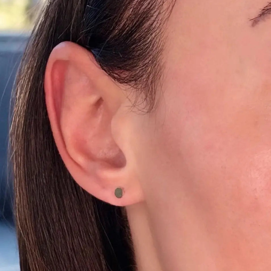 A close-up image of a woman's ear wearing a gold-filled disc stud earring.