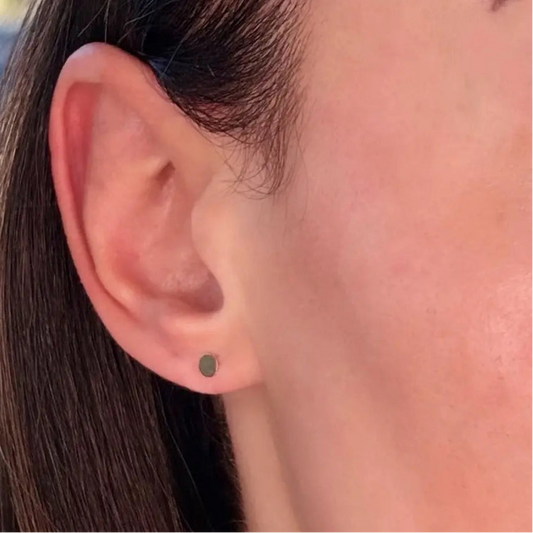 A close-up image of a woman's ear wearing a gold-filled disc stud earring.