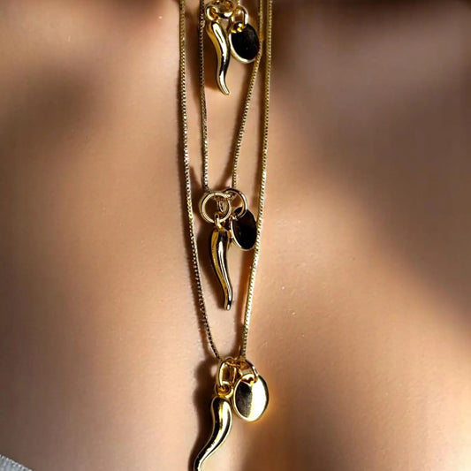 A close-up image of a woman's neck wearing a gold-colored necklace with an Italian horn pendant & small go disc pendant.