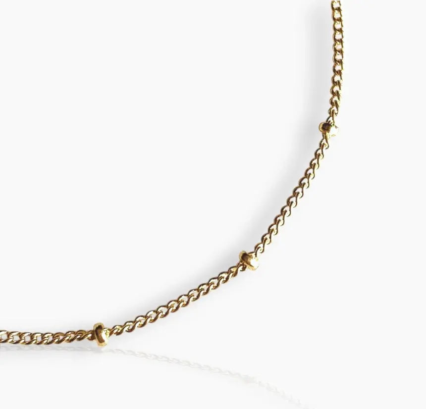 A close-up image of  gold-filled bracelet with small beads strung along a fine chain on a white background