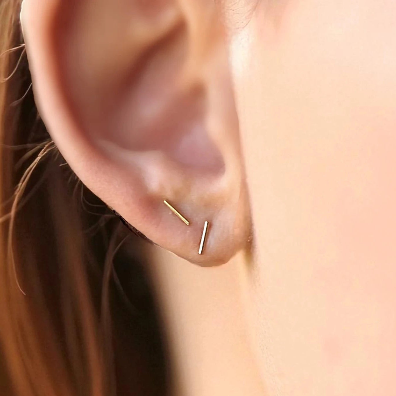 Close-up of an ear wearing a gold bar stud earring with blurred background