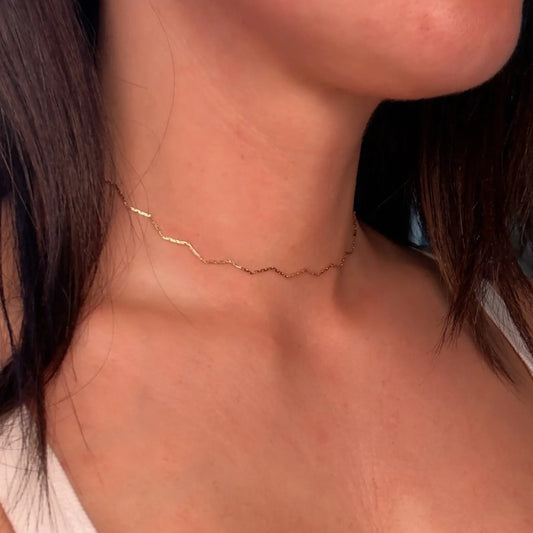 A close-up image of a person wearing a gold-filled chain choker necklace with a zigzag design.