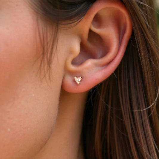 Close-up of an ear wearing a gold triangle-shaped earring with blurred background