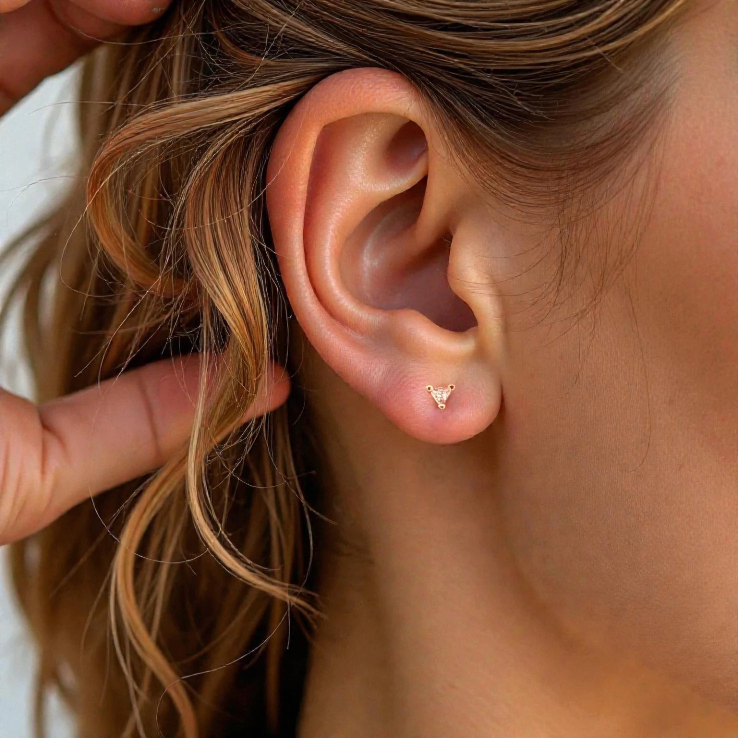 Close-up of an ear with a gold earring, held by a hand.