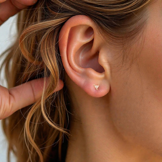 Close-up of an ear with a gold earring, held by a hand.