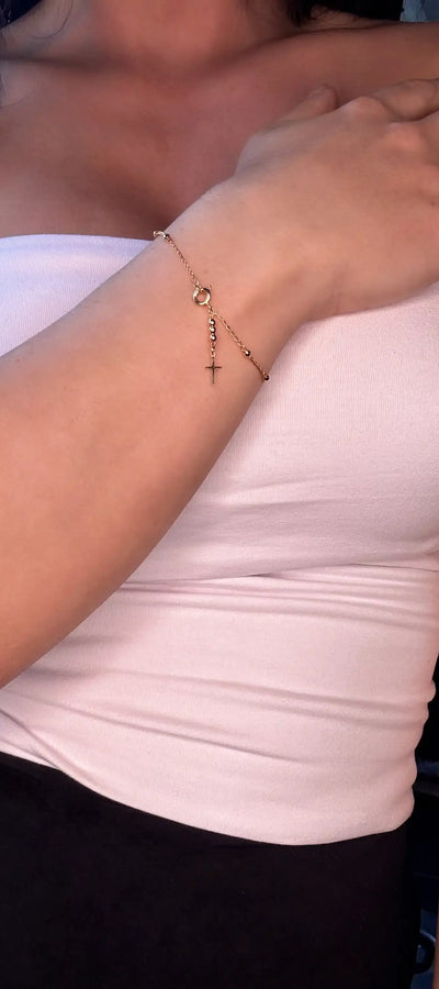 A person wearing a white strapless top showcasing a gold cross bracelet on their wrist.