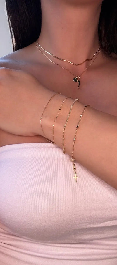 A person wearing a white tank top showcasing gold-colored box chain bracelets on their forearm.