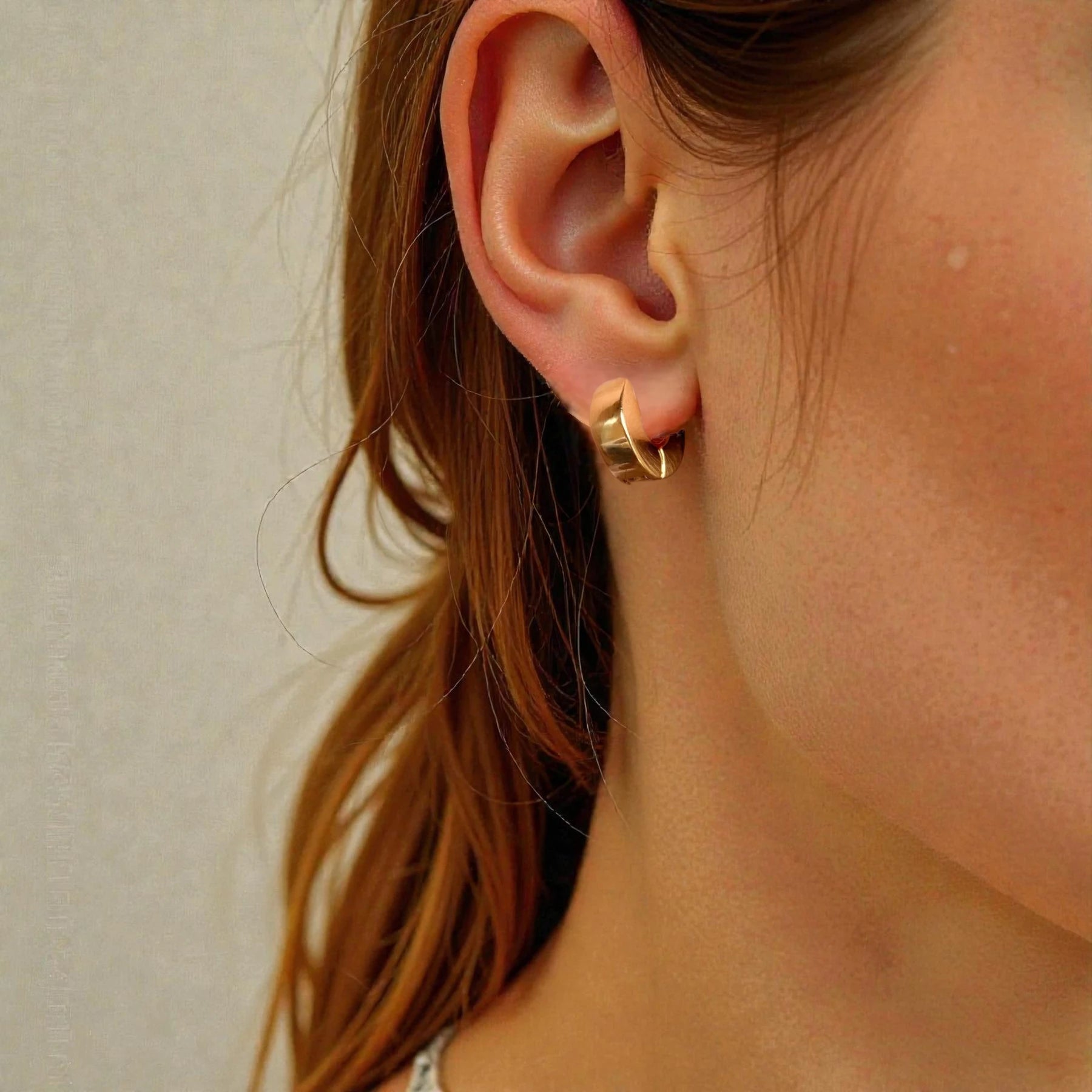 Close-up of a person wearing a gold hoop earring with a neutral background
