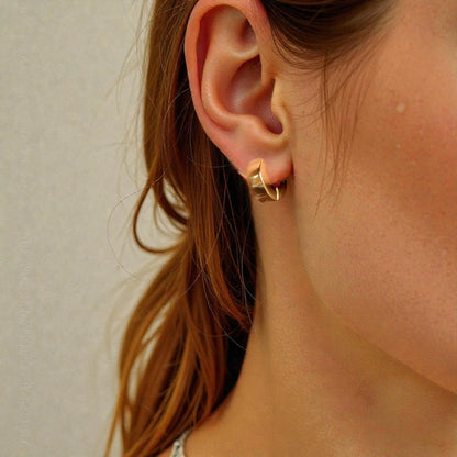 Close-up of a person wearing a gold hoop earring with a neutral background