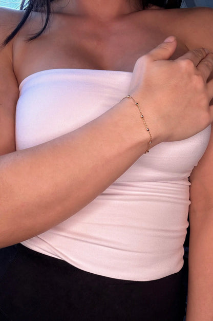 Blessed Gold Cross Bracelet gold bracelet styled on wrist. Bracelet has small ball and chain feature 