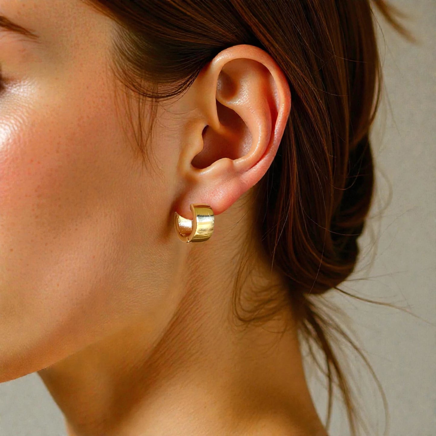 Close-up of a person wearing a gold hoop earring with a neutral background