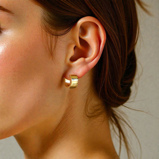Close-up of a person wearing a gold hoop earring with a neutral background