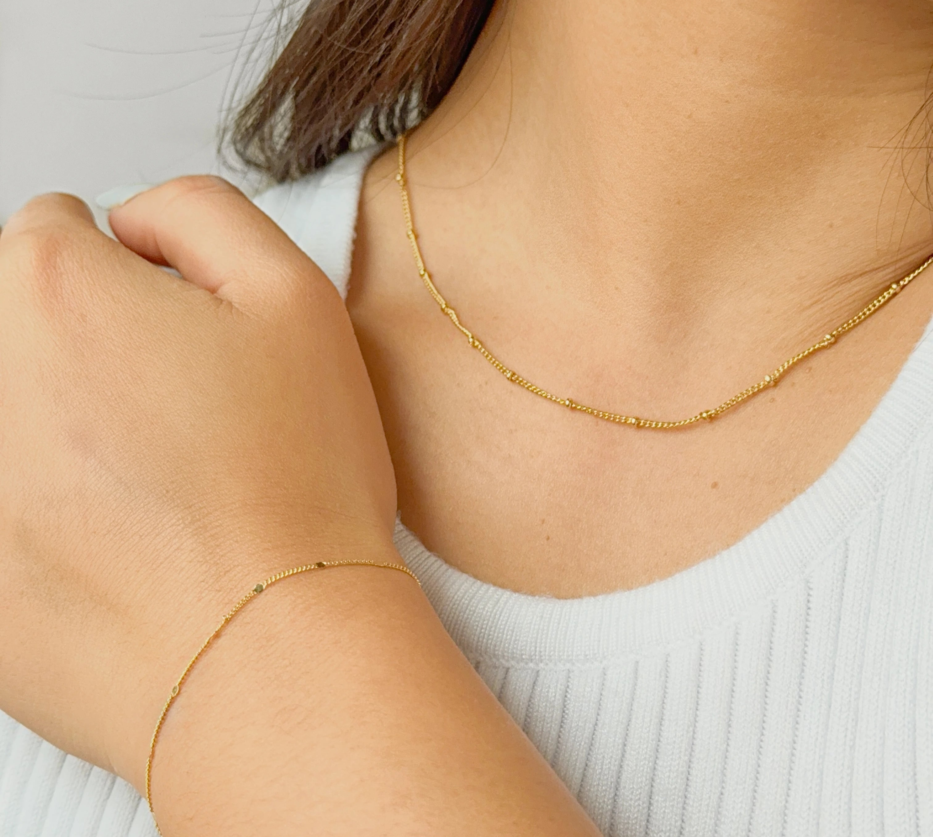 Gold bracelet and necklace on a person wearing a white top