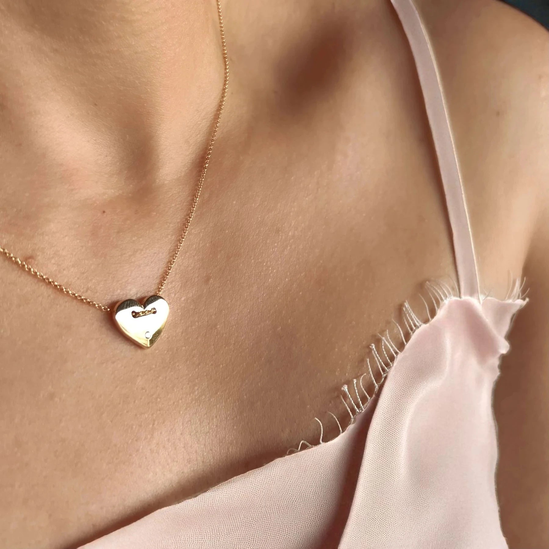Gold heart-shaped necklace on a person wearing a light pink top.