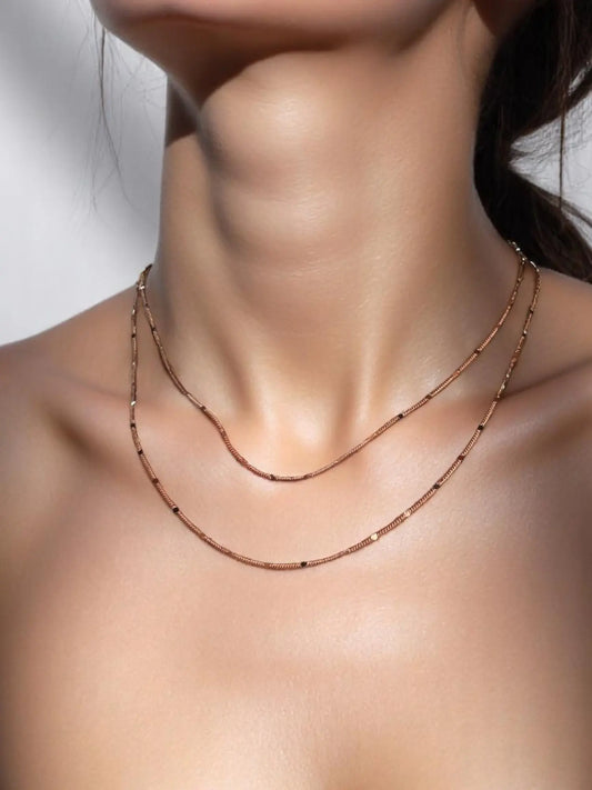A close-up image of a woman's neck wearing a gold-filled curb chain necklace with a pressed detail.