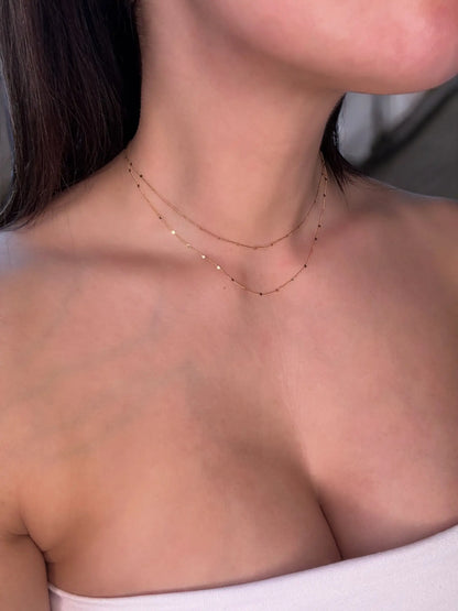 Close-up of a person wearing a delicate gold necklace on a neutral background
