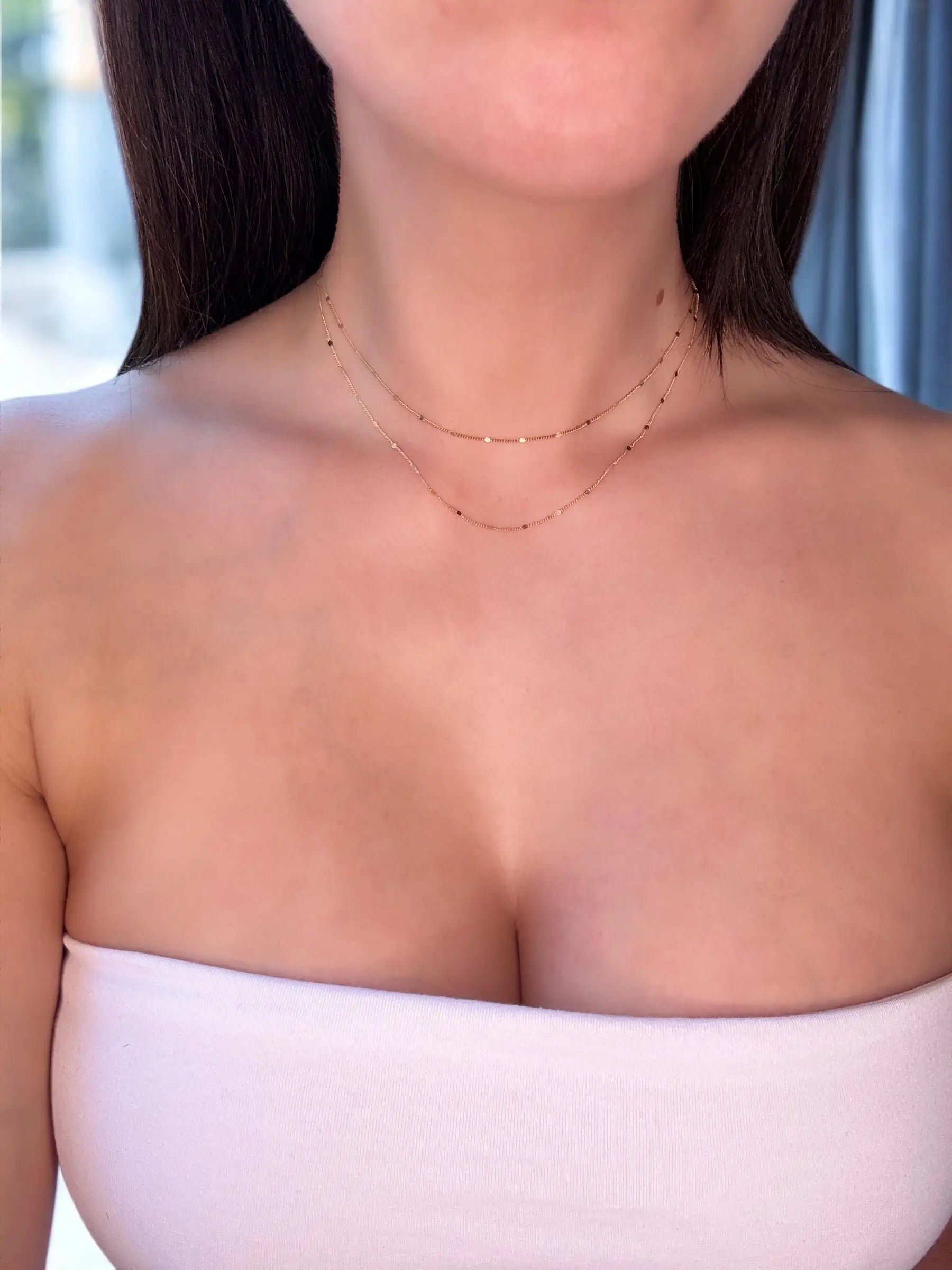 Close-up of a person wearing a delicate necklace with a white top 