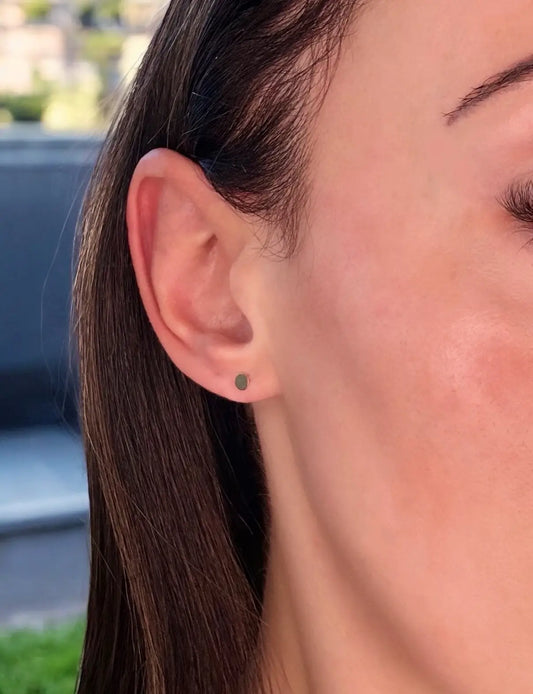 A close-up image of a woman's ear wearing a gold-filled disc stud earring.
