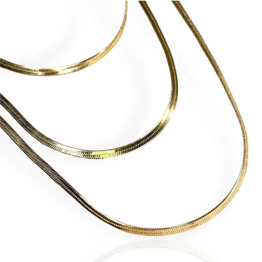 A gold herringbone chain necklace laid out on a plain surface.