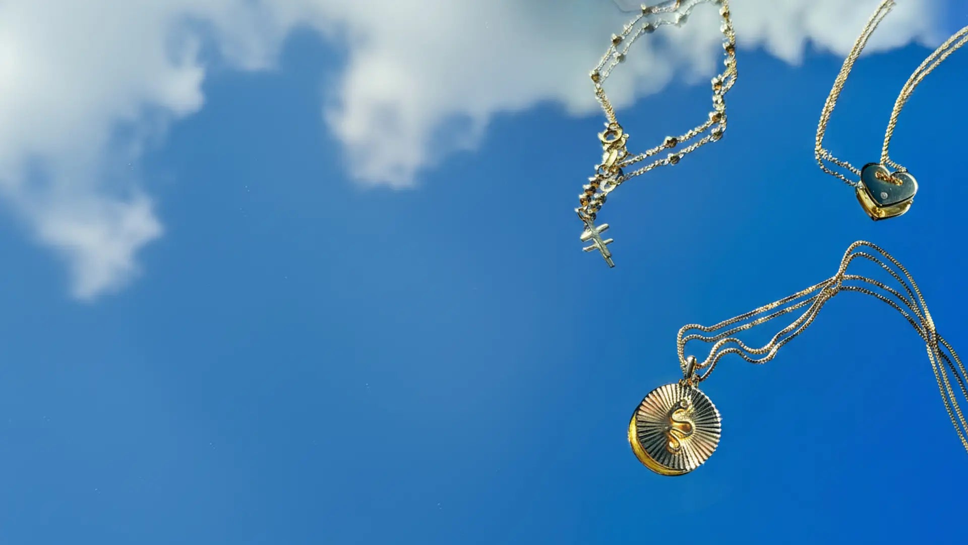 blue sky with clouds with a snake pendant medal necklace and heart with diamond and cross charm bracelet with ball chain 
