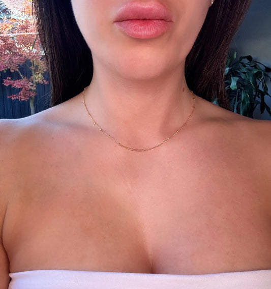 Close-up of a person wearing a delicate gold necklace with a satelite detail 