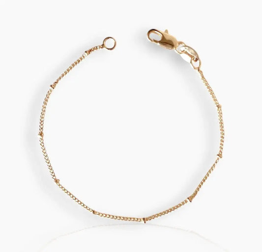 A close-up image of  gold-filled bracelet with small beads strung along a fine chain on a white background 