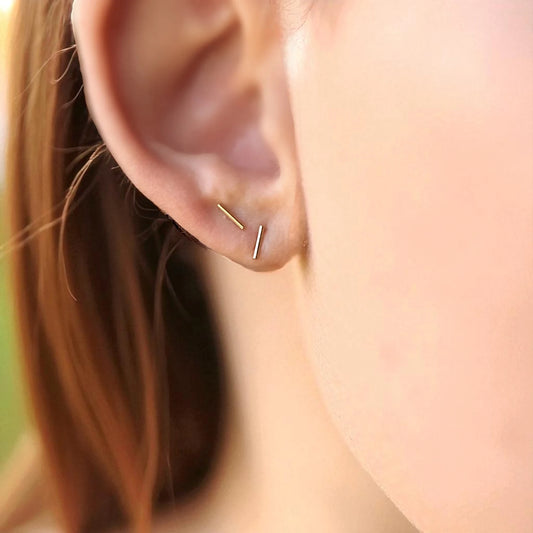 Close-up of an ear wearing a gold bar stud earring with blurred background